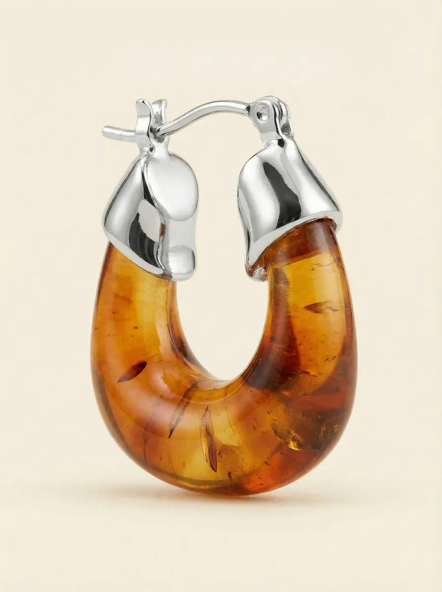 Silver hoop earring with a large curved amber drop on a cream background