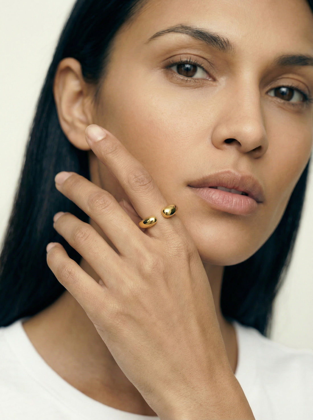 Sap Ring, gold-tone open ring with rounded ends, worn on a woman's hand resting against her cheek