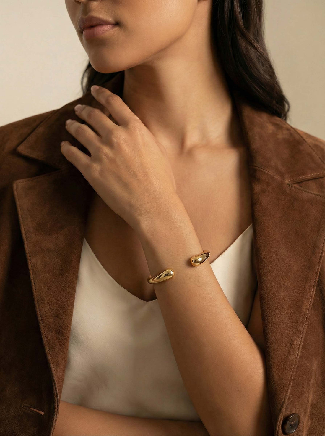 Arc Cuff, gold-tone open cuff worn on a woman's wrist, her other hand resting near her shoulder