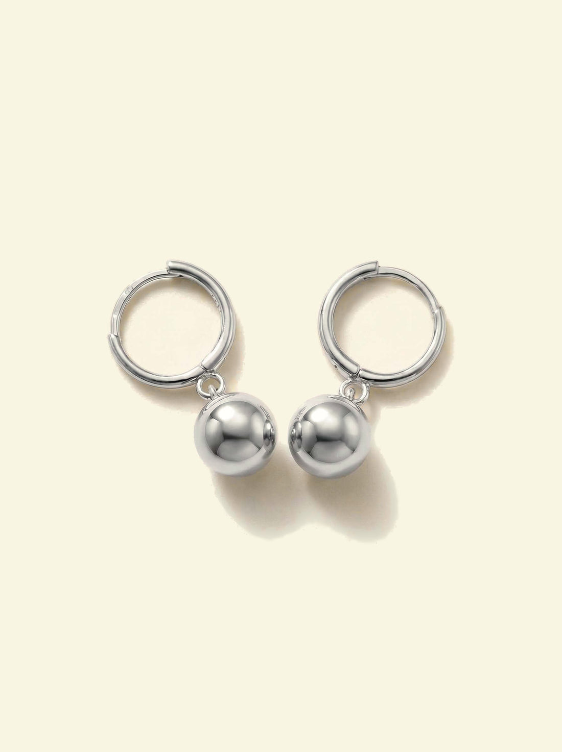 Dawn Drops, pair of silver-tone huggie hoops with ball drops, angled view with soft shadows