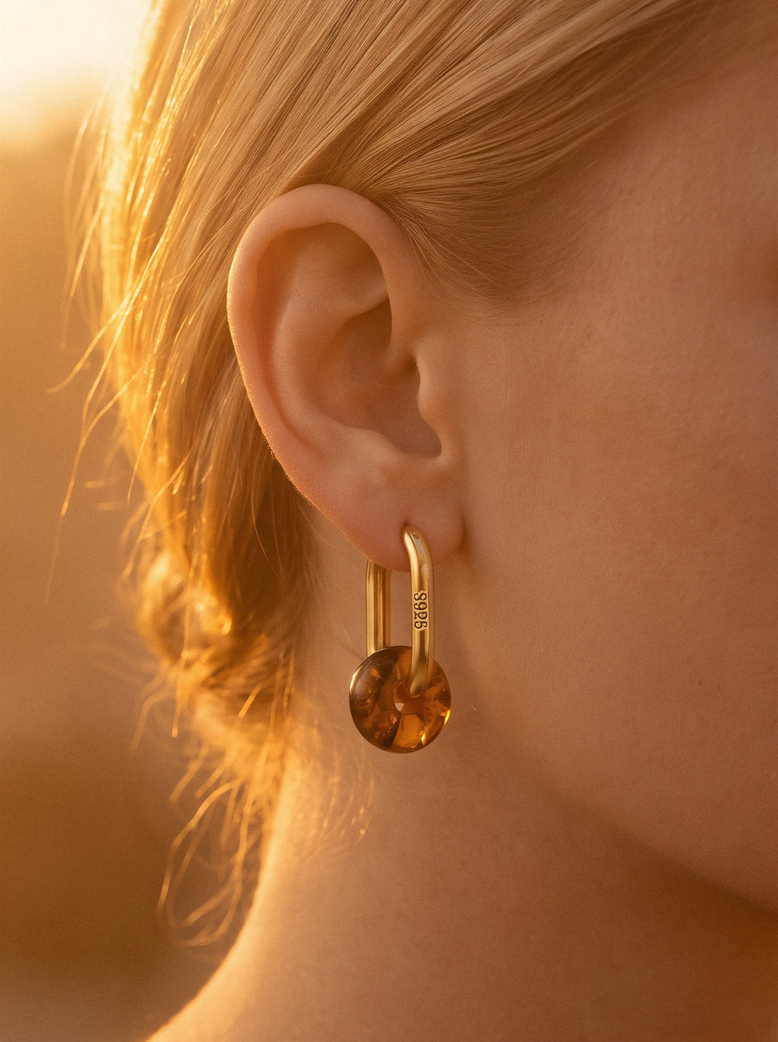Dune Amber Hoops, gold-tone oval hoop with an amber-coloured bead worn on a woman's ear, side view