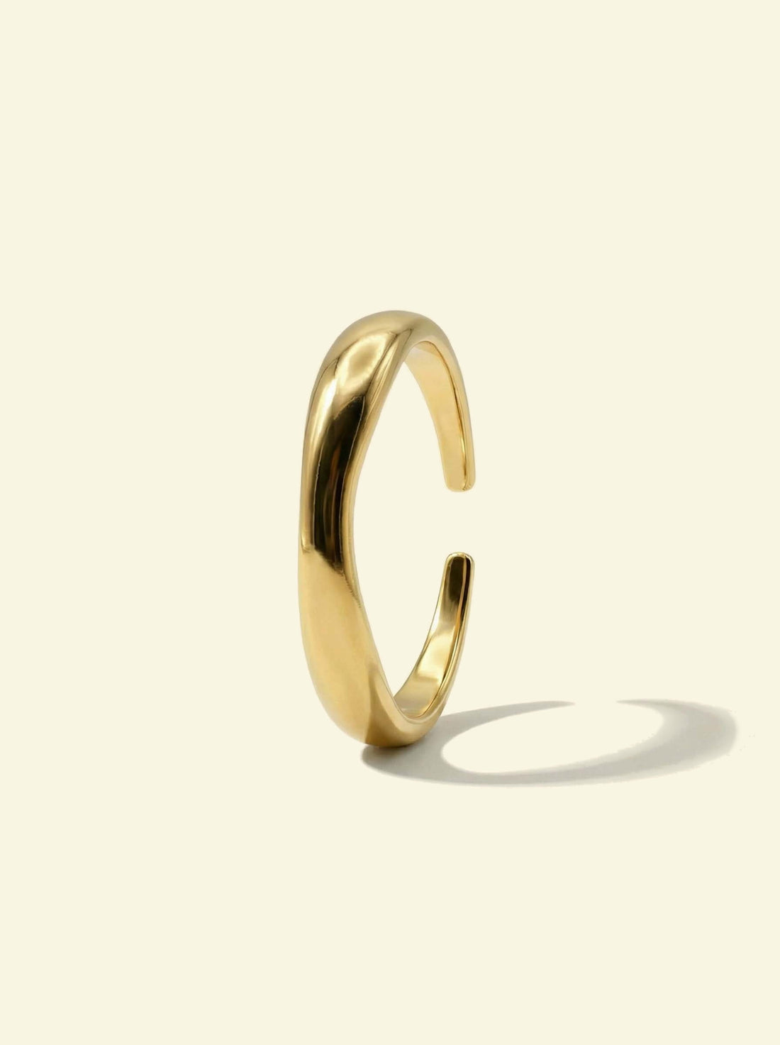 River Ring, gold-tone open wavy band standing upright, side view with a long shadow