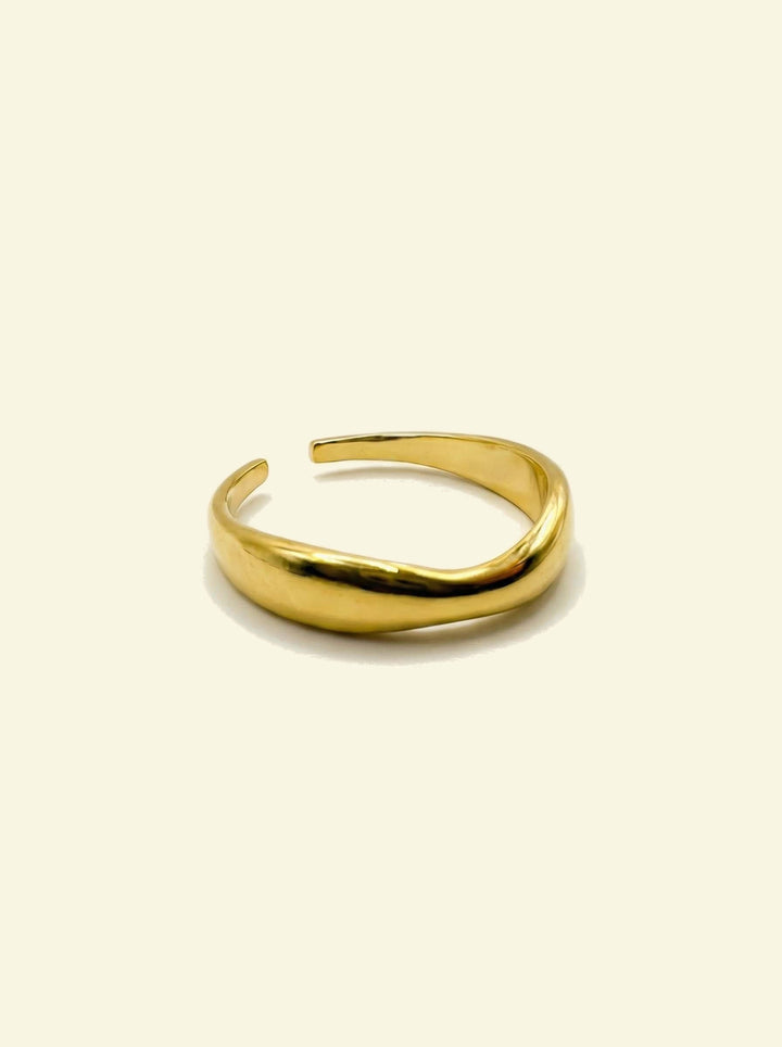 River Ring, gold-tone open wavy band, three-quarter view on a cream background