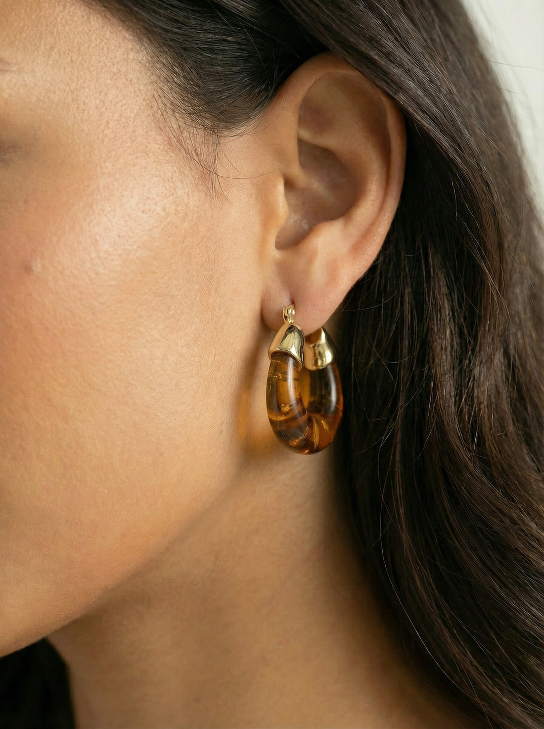 Ember Hoops, translucent amber-coloured hoop with a gold-tone cap worn on a woman's ear, side view