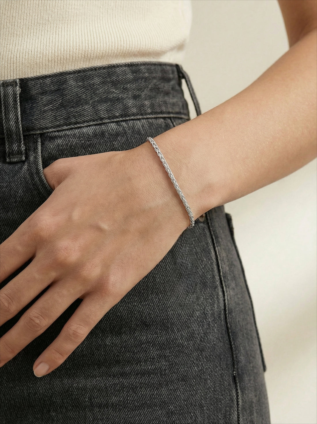 Essential Chain Bracelet, silver-tone braided chain worn on a woman's wrist, hand resting in a denim pocket
