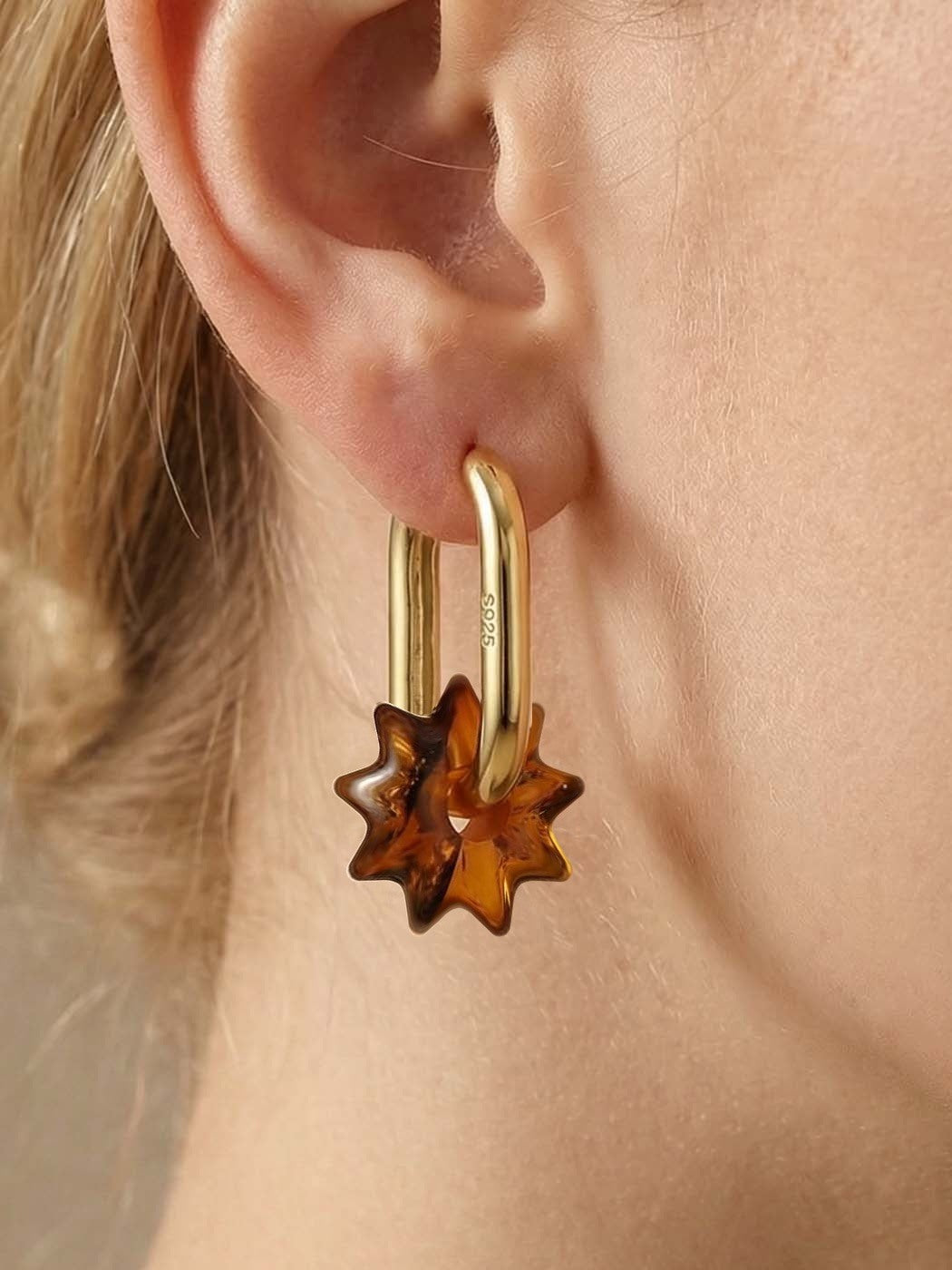 Dune Noon Amber Hoops, close-up of a sun-shaped charm of honey-brown amber on a gold-tone tall oval hoop, worn on a woman's ear