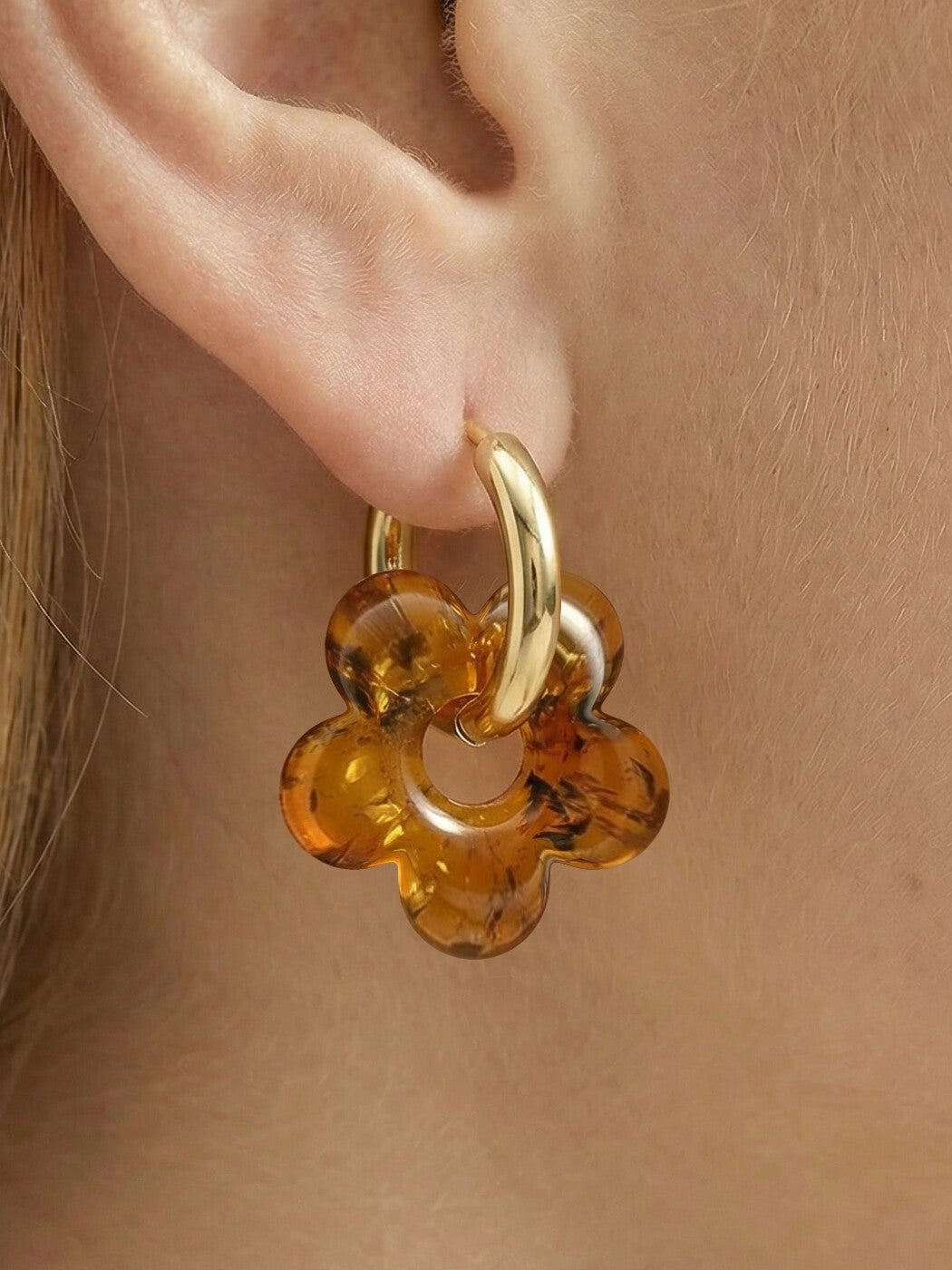 Nida Bloom Amber Hoops, close-up of a five-petal flower charm of honey-brown amber on a gold-tone huggie hoop, worn on a woman's ear