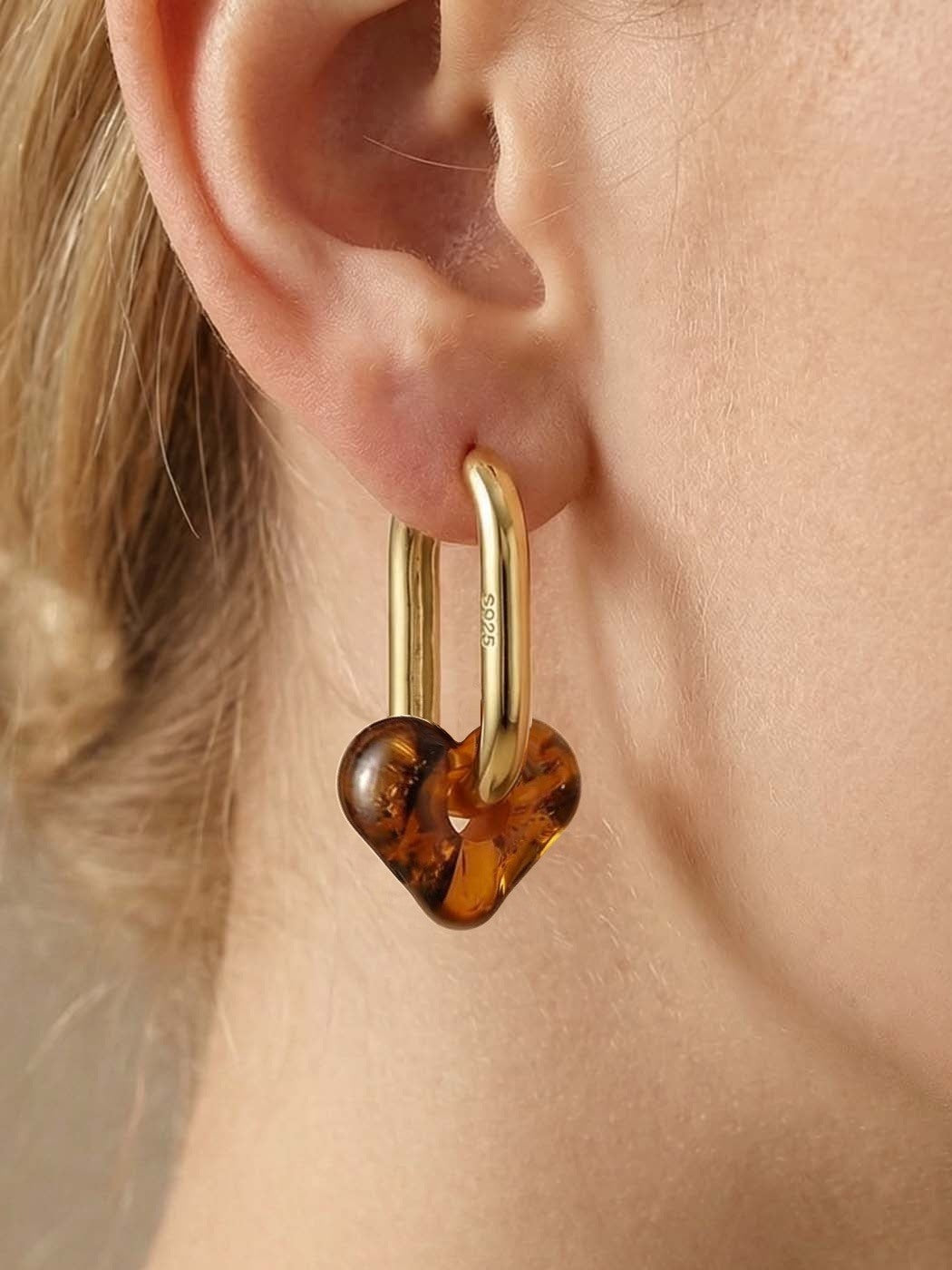 Dune Haven Amber Hoops, close-up of a soft heart-shaped charm of honey-brown amber on a gold-tone tall oval hoop, worn on a woman's ear