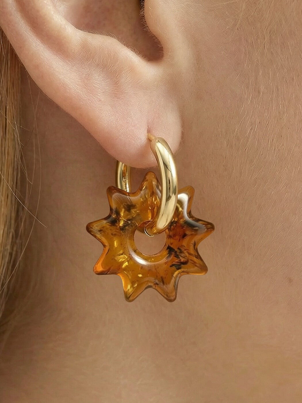 Nida Noon Amber Hoops, close-up of a sun-shaped charm of honey-brown amber on a gold-tone huggie hoop, worn on a woman's ear