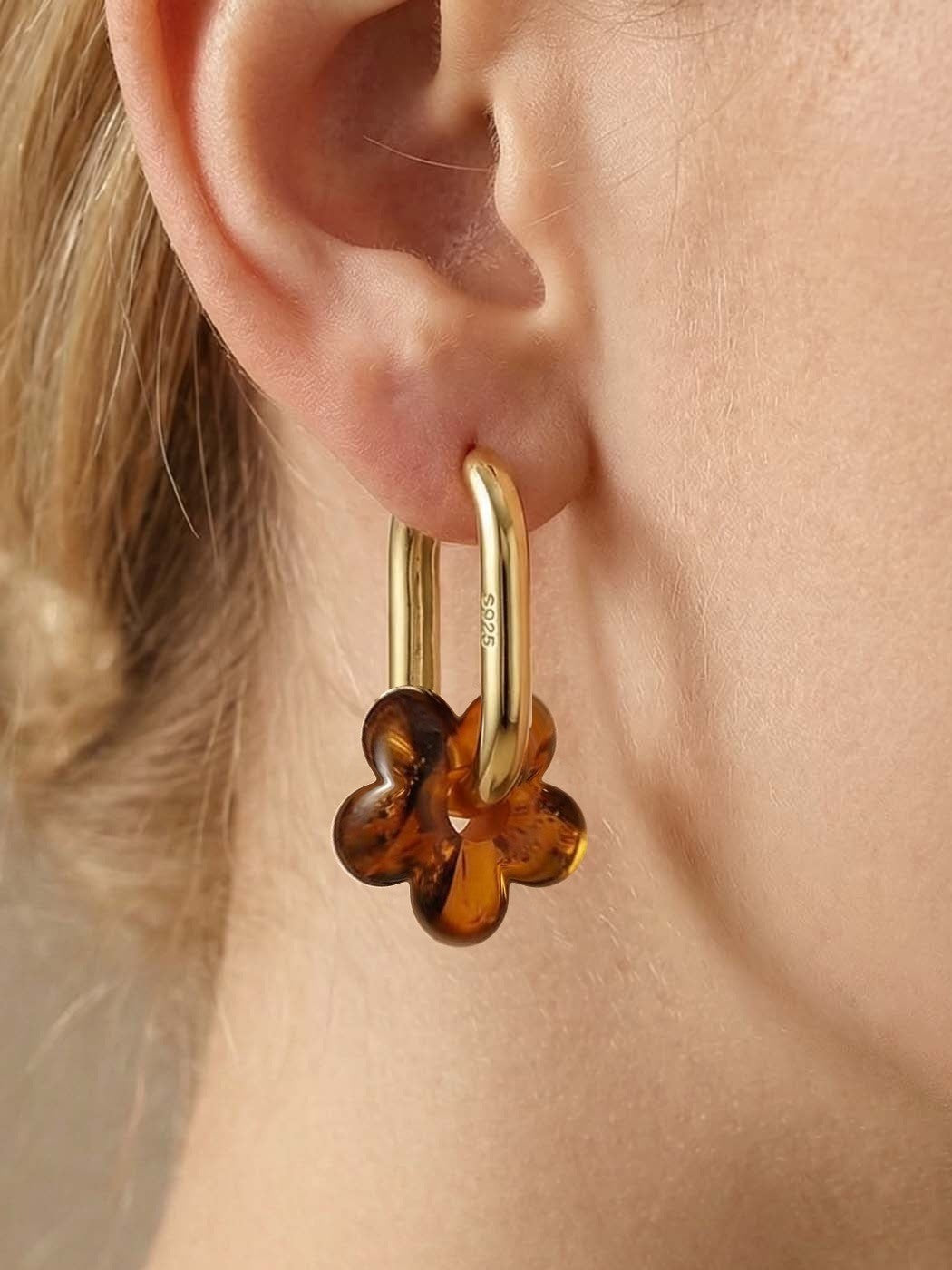 Dune Bloom Amber Hoops, close-up of a five-petal flower charm of honey-brown amber on a gold-tone tall oval hoop, worn on a woman's ear