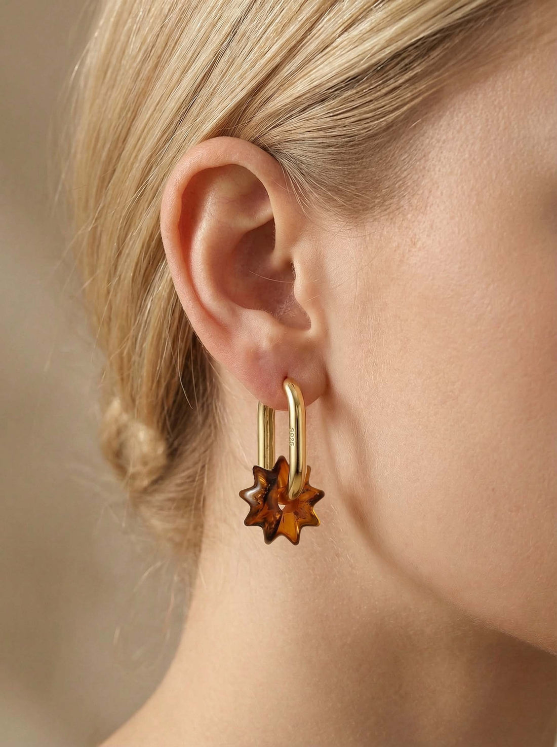 Dune Noon Amber Hoops, gold-tone tall oval hoop with a sun-shaped charm of honey-brown amber, worn on a woman's ear