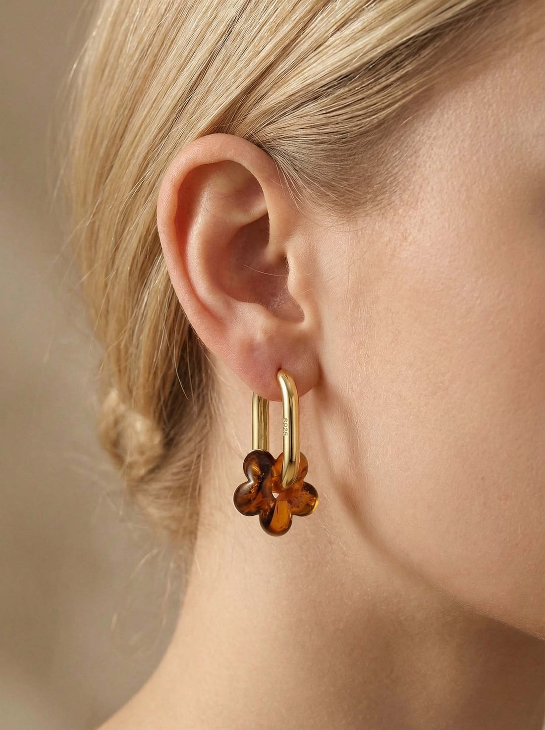 Dune Bloom Amber Hoops, gold-tone tall oval hoop with a five-petal flower charm of honey-brown amber, worn on a woman's ear