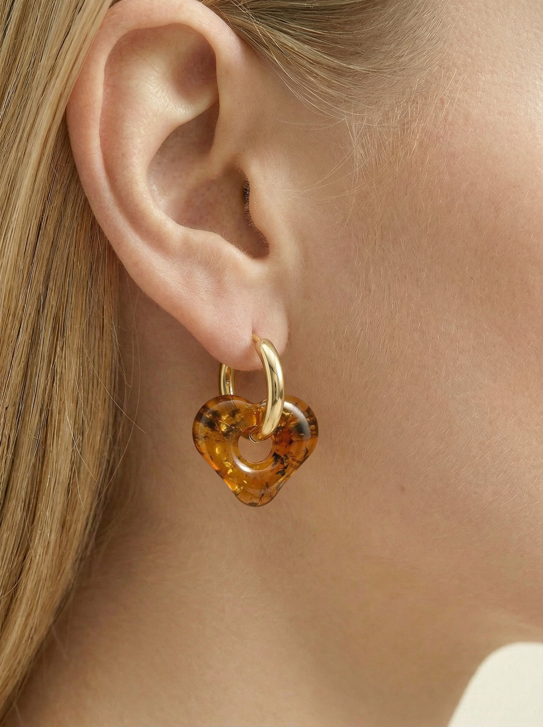 Nida Haven Amber Hoops, gold-tone huggie hoop with a soft heart-shaped charm of honey-brown amber, worn on a woman's ear