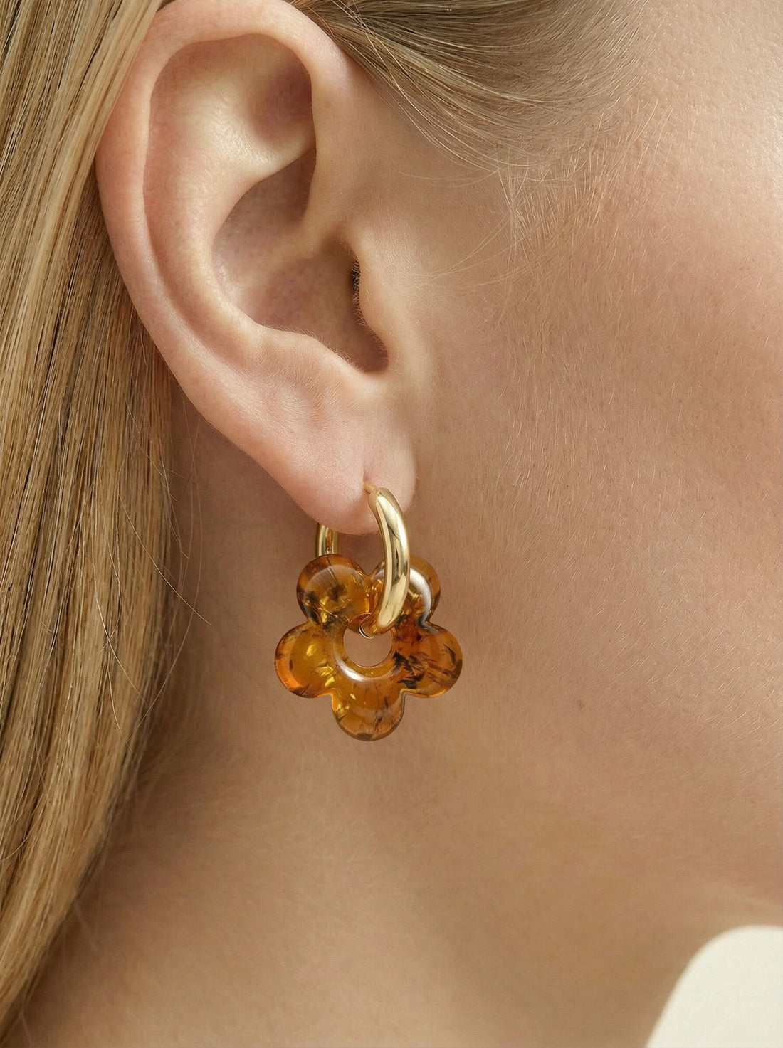Nida Bloom Amber Hoops, gold-tone huggie hoop with a five-petal flower charm of honey-brown amber, worn on a woman's ear