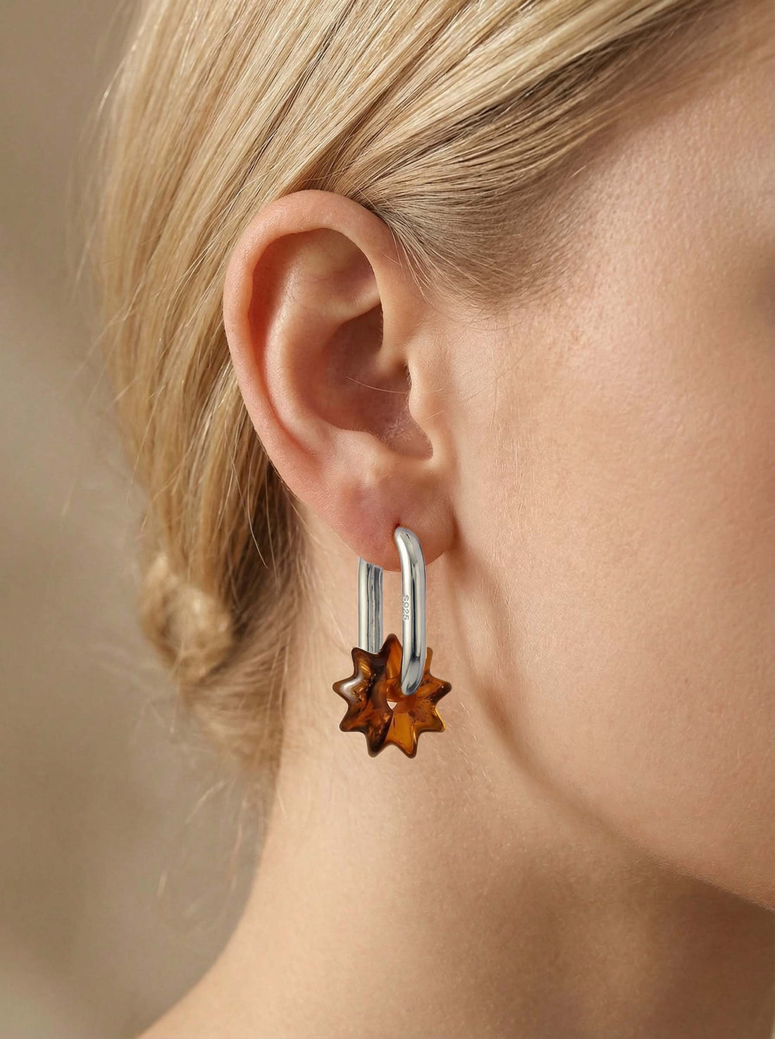 Dune Noon Amber Hoops, silver-tone tall oval hoop with a sun-shaped charm of honey-brown amber, worn on a woman's ear