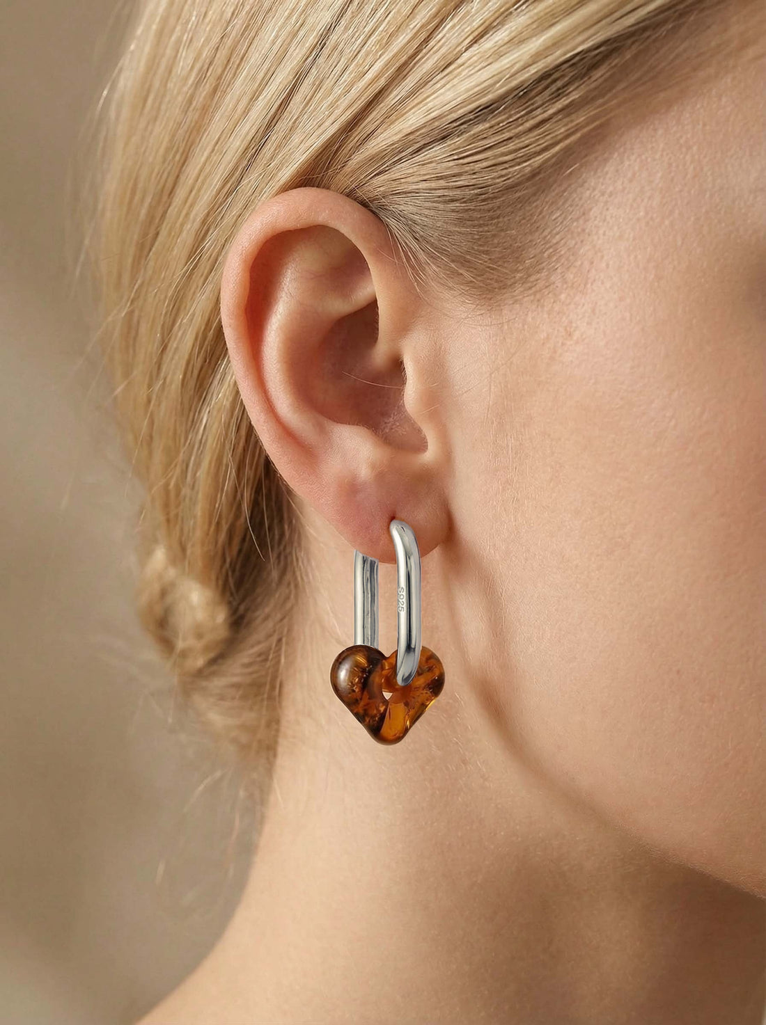 Dune Haven Amber Hoops, silver-tone tall oval hoop with a soft heart-shaped charm of honey-brown amber, worn on a woman's ear