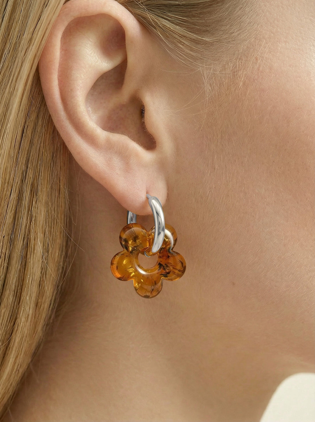 Nida Bloom Amber Hoops, silver-tone huggie hoop with a five-petal flower charm of honey-brown amber, worn on a woman's ear