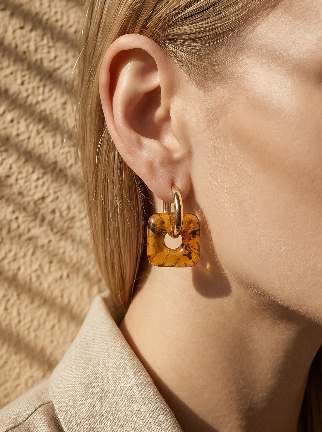 Nida Lantern Amber Hoops, gold-tone huggie hoop with a rounded square charm of honey-brown amber, worn on a woman's ear