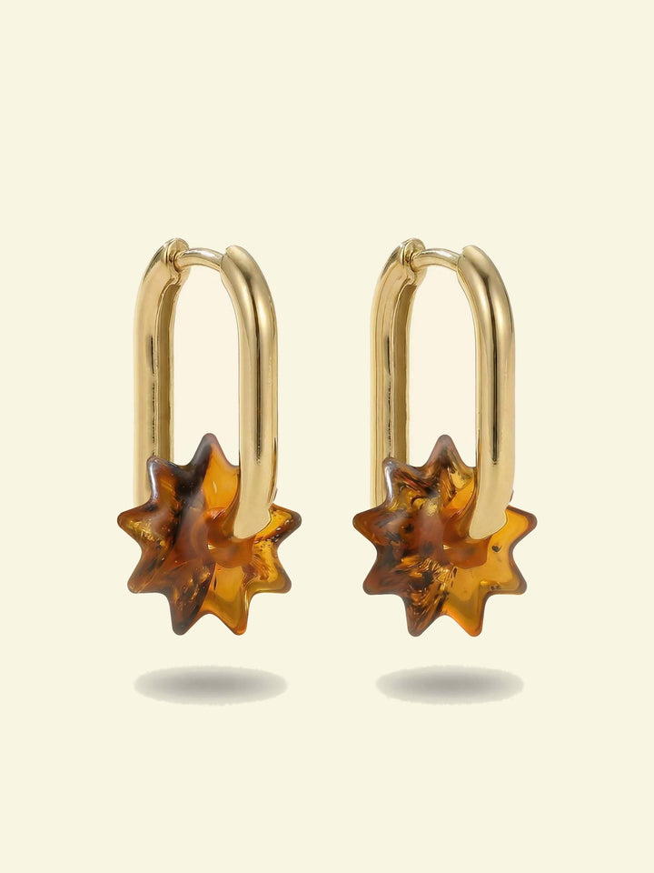 Dune Noon Amber Hoops, pair of gold-tone tall oval hoops with sun-shaped charms of honey-brown amber, front view on a cream background