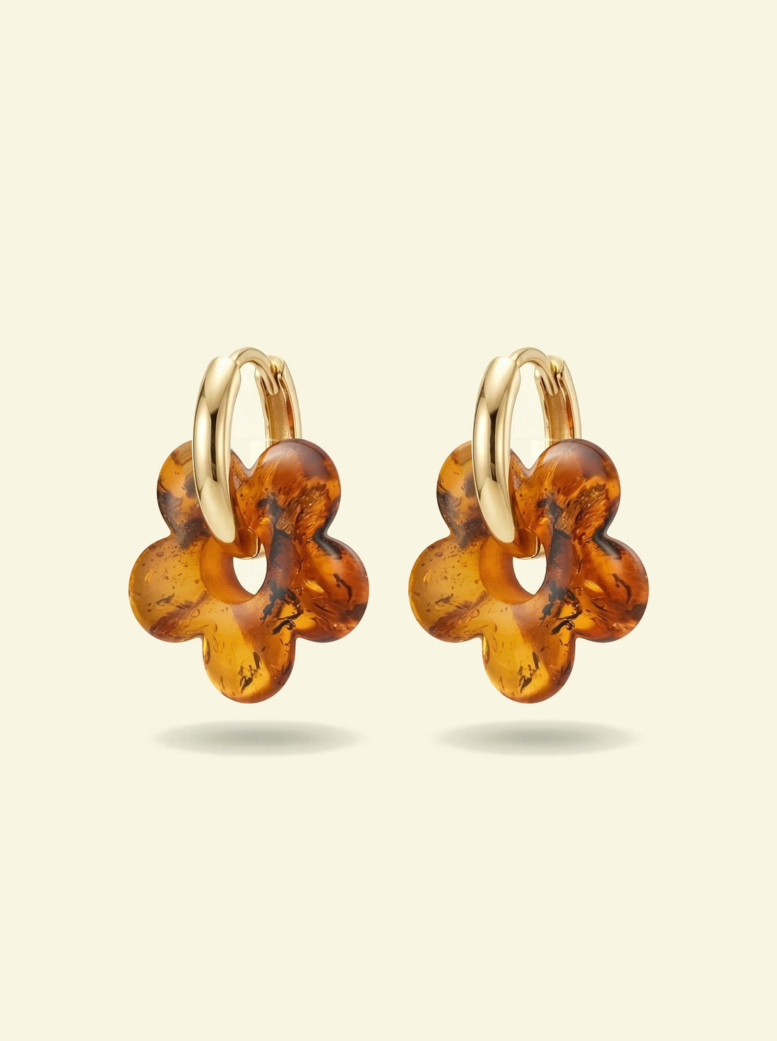 Nida Bloom Amber Hoops, pair of gold-tone huggie hoops with five-petal flower charms of honey-brown amber, front view on a cream background