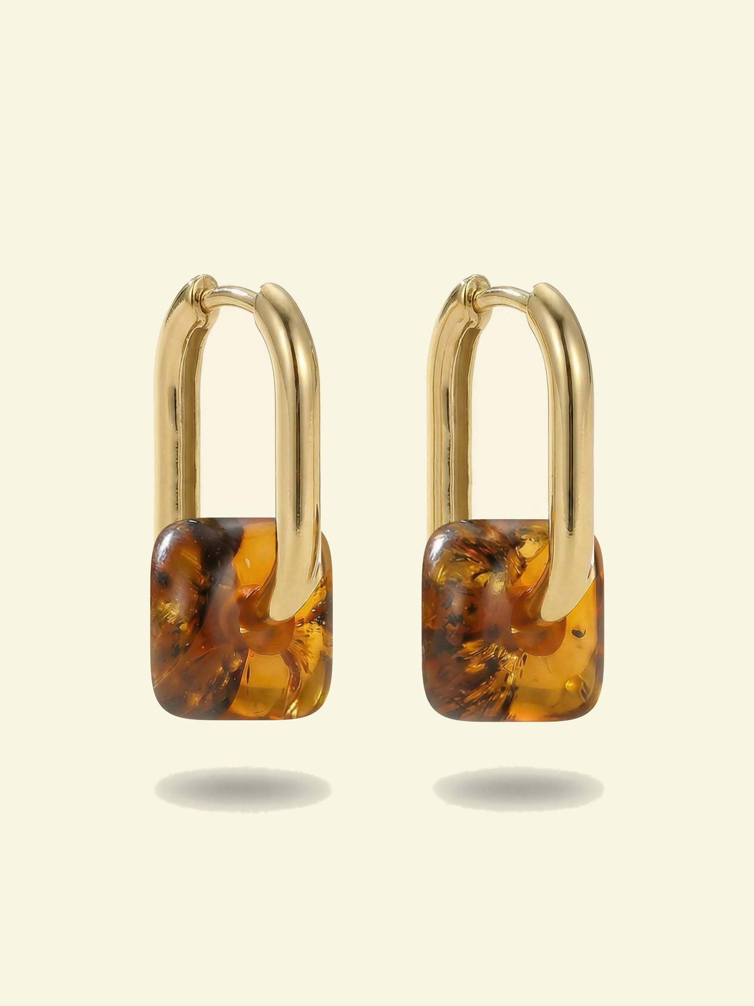 Dune Lantern Amber Hoops, pair of gold-tone tall oval hoops with rounded square charms of honey-brown amber, front view on a cream background