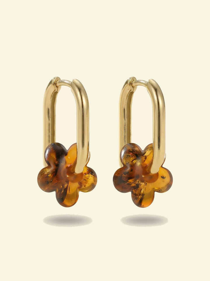Dune Bloom Amber Hoops, pair of gold-tone tall oval hoops with five-petal flower charms of honey-brown amber, front view on a cream background