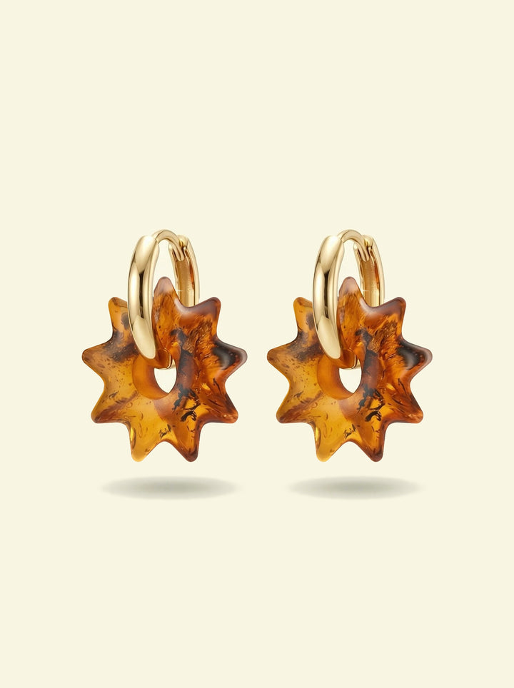 Nida Noon Amber Hoops, pair of gold-tone huggie hoops with sun-shaped charms of honey-brown amber, front view on a cream background