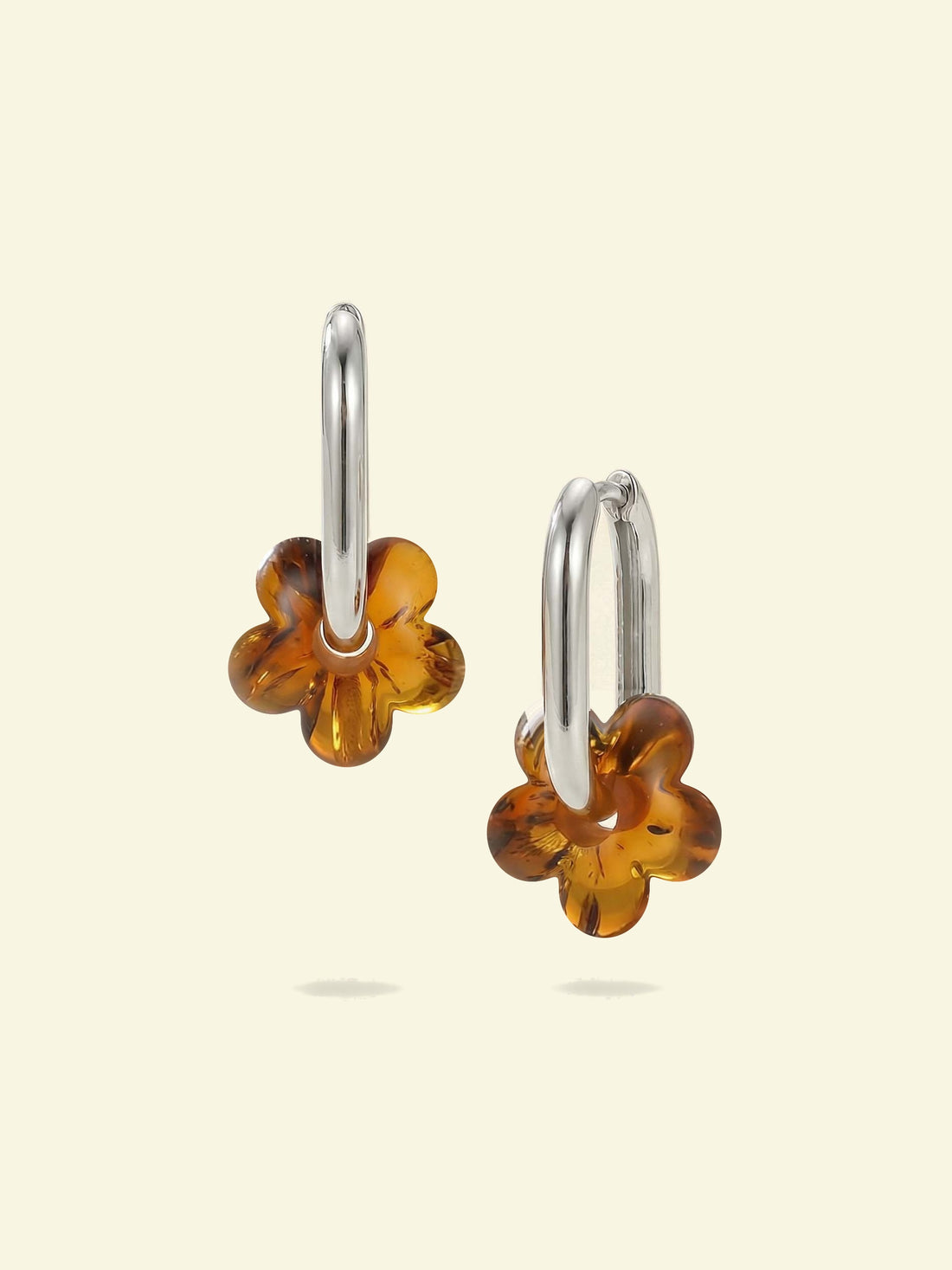 Dune Bloom Amber Hoops, pair of silver-tone tall oval hoops with five-petal flower charms of honey-brown amber, front view on a cream background