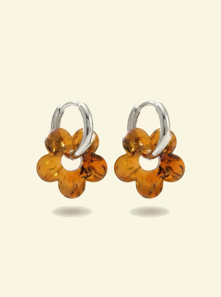 Nida Bloom Amber Hoops, pair of silver-tone huggie hoops with five-petal flower charms of honey-brown amber, front view on a cream background