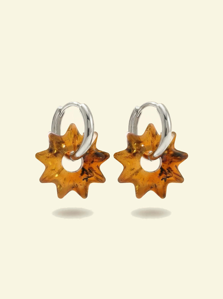 Nida Noon Amber Hoops, pair of silver-tone huggie hoops with sun-shaped charms of honey-brown amber, front view on a cream background
