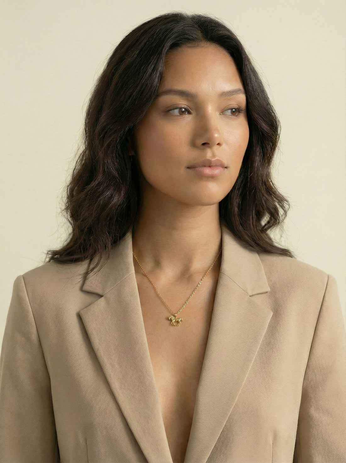 Stallion Pendant, gold-tone horse pendant on a fine chain worn at a woman's neckline with a beige blazer