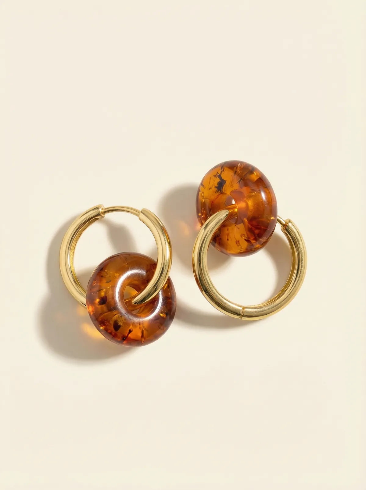 Pair of gold hoop earrings, each with a round amber bead, on a cream background